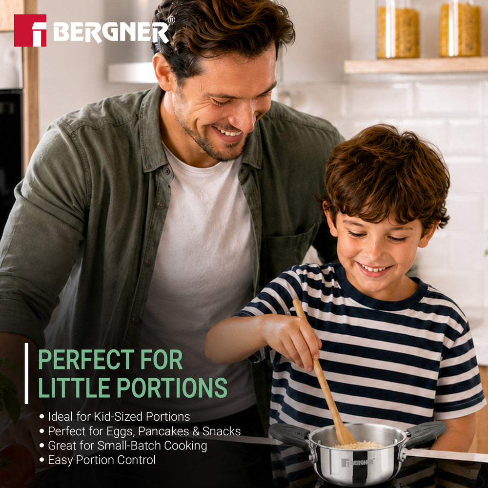 A man and a young boy smiling while cooking together in a bright kitchen. The boy is stirring a small stainless steel pot with a wooden spoon.