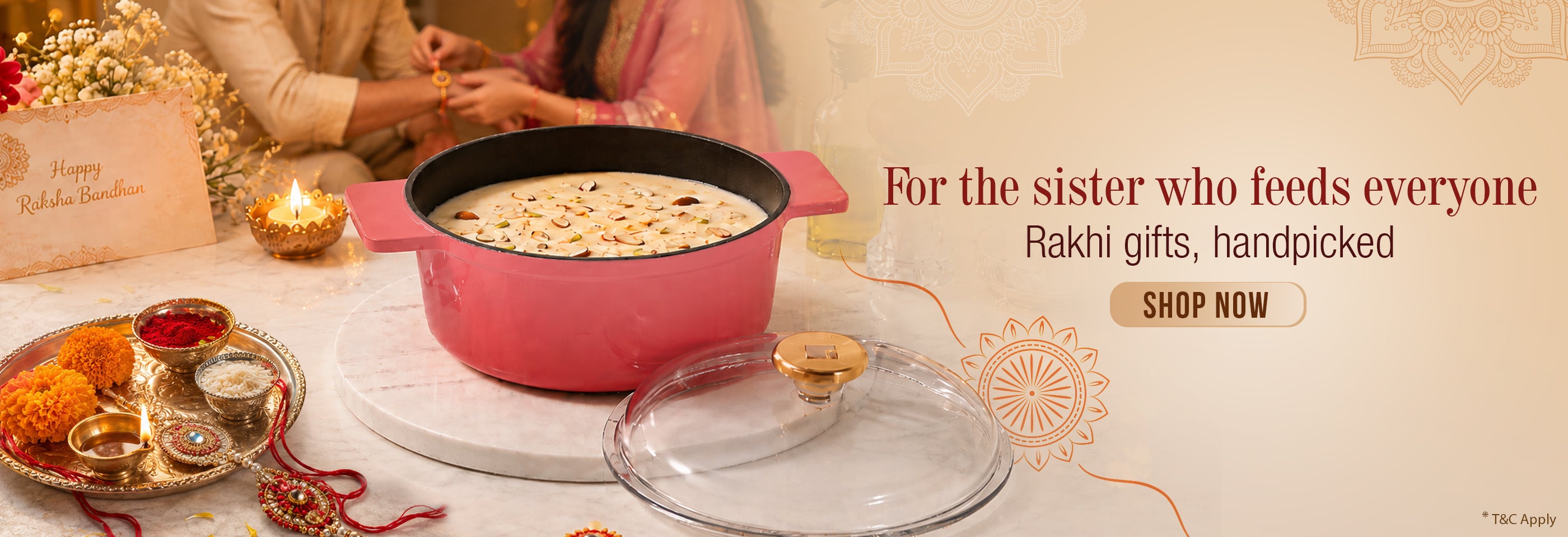 A pink Excalibur cast-iron casserole filled with kheer or rice pudding, displayed on a white marble tray with a glass lid, alongside traditional Indian festive items like a brass lamp, marigold flowers, and a Rakhi. The background shows a festive celebration with siblings, and the text reads 'For the sister who feeds everyone Rakhi gifts, handpicked SHOP NOW'.