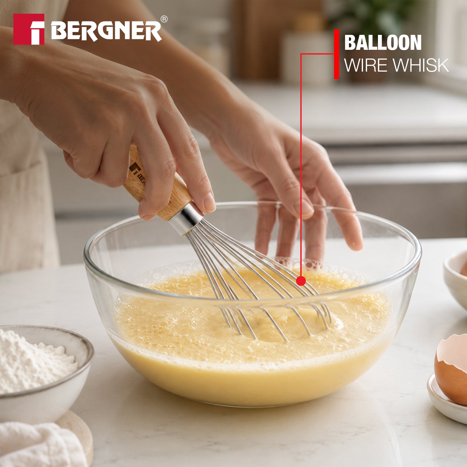 Bergner Essential Plus 20cm manual hand whisk with wooden handle beating batter in a glass bowl, highlighting the balloon wire whisk design